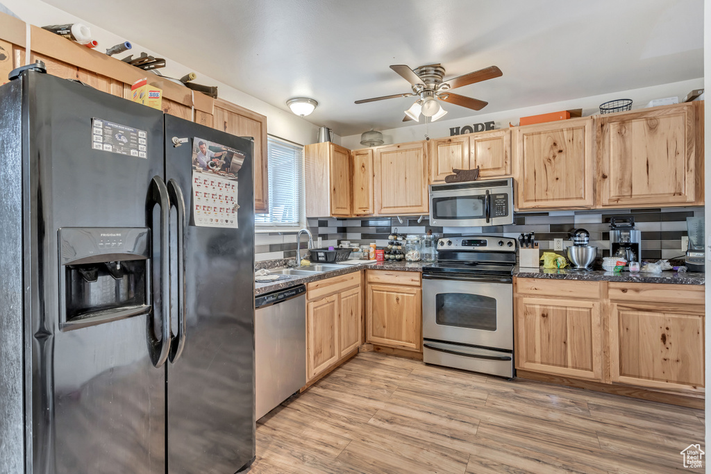 Kitchen with appliances with stainless steel finishes, ceiling fan, sink, light hardwood / wood-style floors, and backsplash