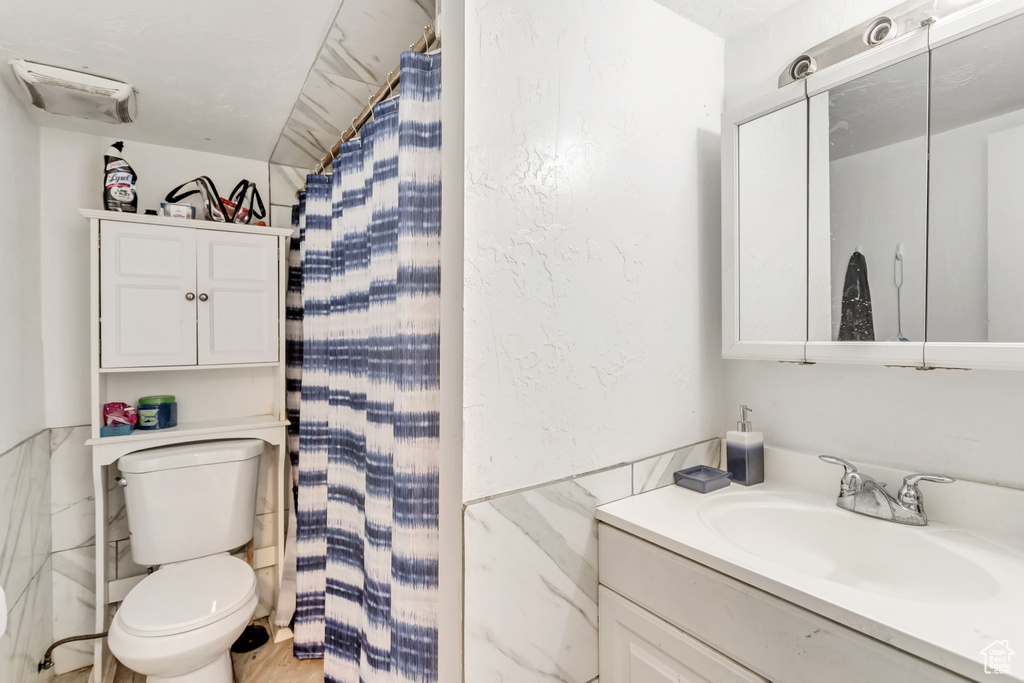 Bathroom featuring vanity, toilet, and tile walls