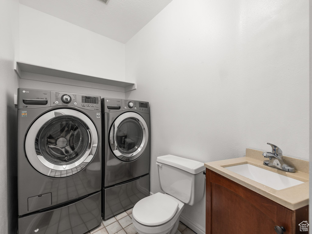 Clothes washing area with sink, independent washer and dryer, and light tile floors