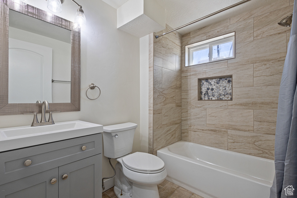Full bathroom featuring vanity with extensive cabinet space, shower / bathtub combination with curtain, toilet, and tile flooring