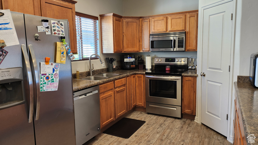 Kitchen with appliances with stainless steel finishes, light hardwood / wood-style flooring, and sink