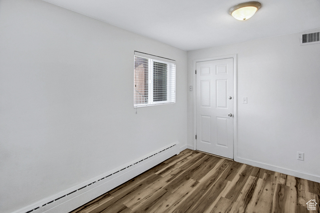 Empty room with wood-type flooring and a baseboard heating unit