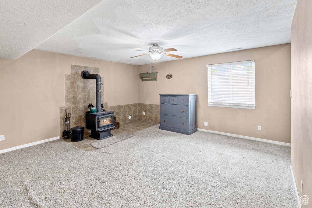 Interior space with a wood stove, carpet flooring, ceiling fan, and a textured ceiling