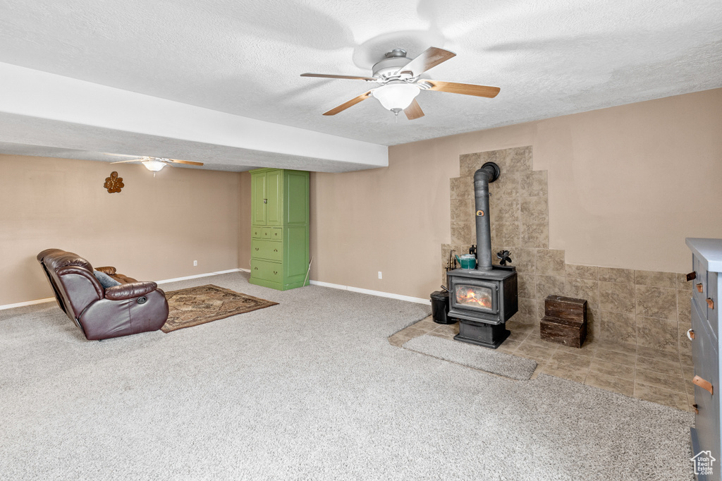 Carpeted living room featuring ceiling fan, tile walls, a wood stove, and a textured ceiling