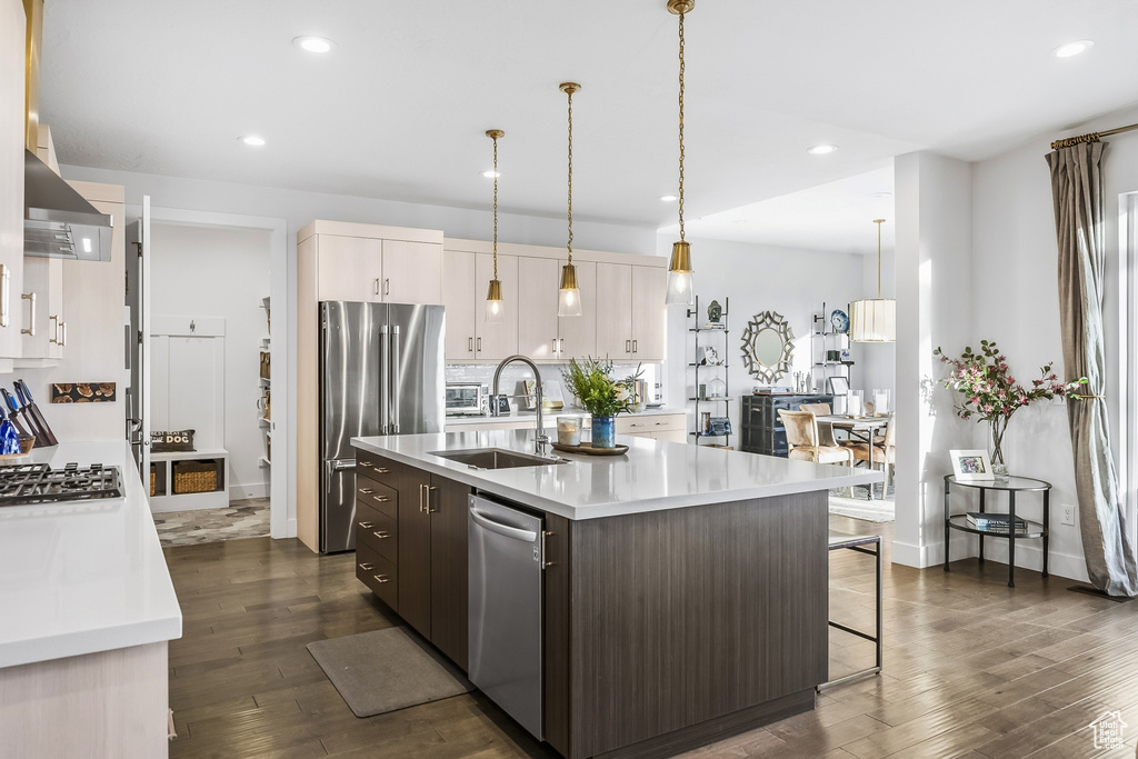 Kitchen with a kitchen island with sink, sink, dark hardwood / wood-style flooring, stainless steel appliances, and pendant lighting