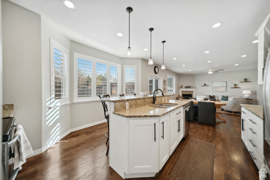 Kitchen featuring a breakfast bar, light stone countertops, dark hardwood / wood-style floors, a center island with sink, and sink