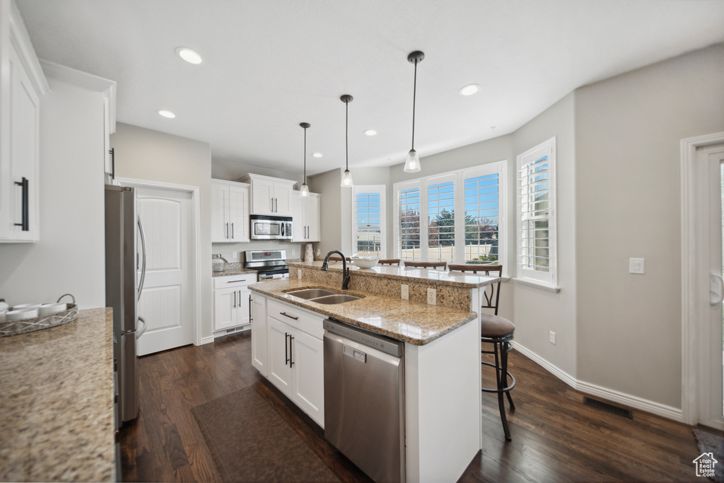 Kitchen with pendant lighting, a breakfast bar, sink, stainless steel appliances, and a kitchen island with sink