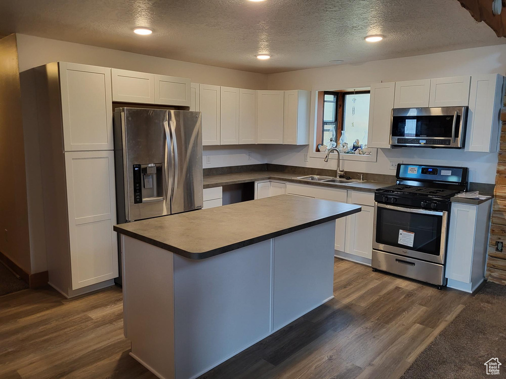 Kitchen with a center island, sink, white cabinetry, stainless steel appliances, and dark hardwood / wood-style floors