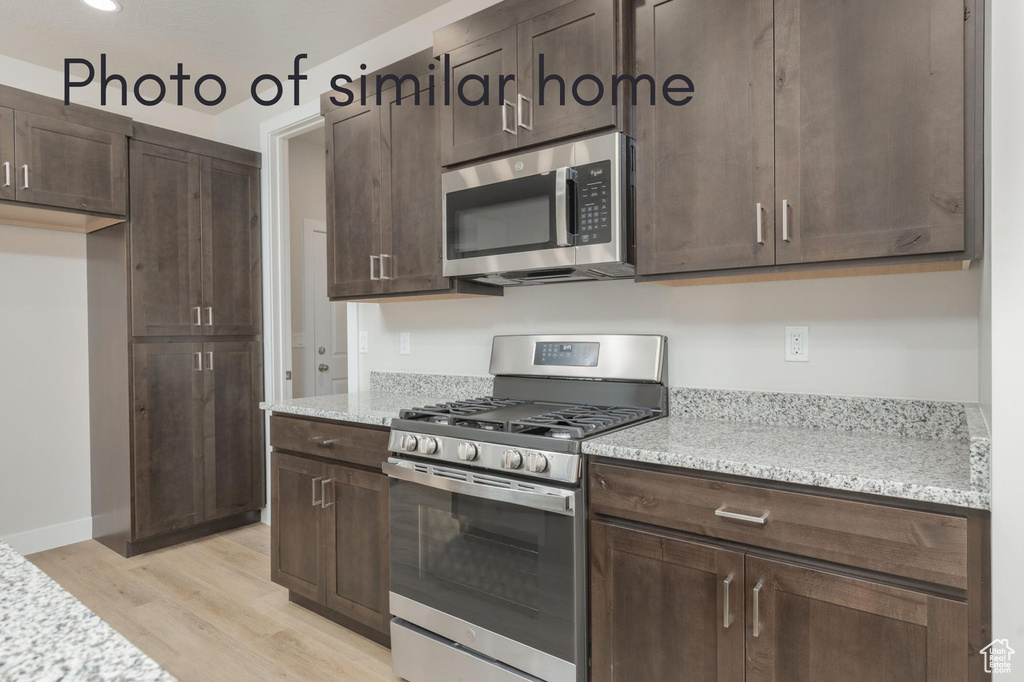 Kitchen featuring appliances with stainless steel finishes, dark brown cabinets, light stone countertops, and light hardwood / wood-style floors