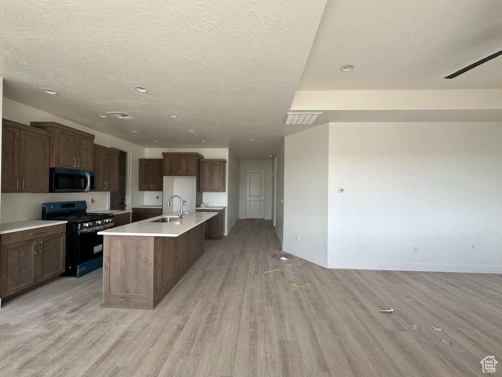 Kitchen with black range with gas stovetop, a center island with sink, sink, light wood-type flooring, and a textured ceiling