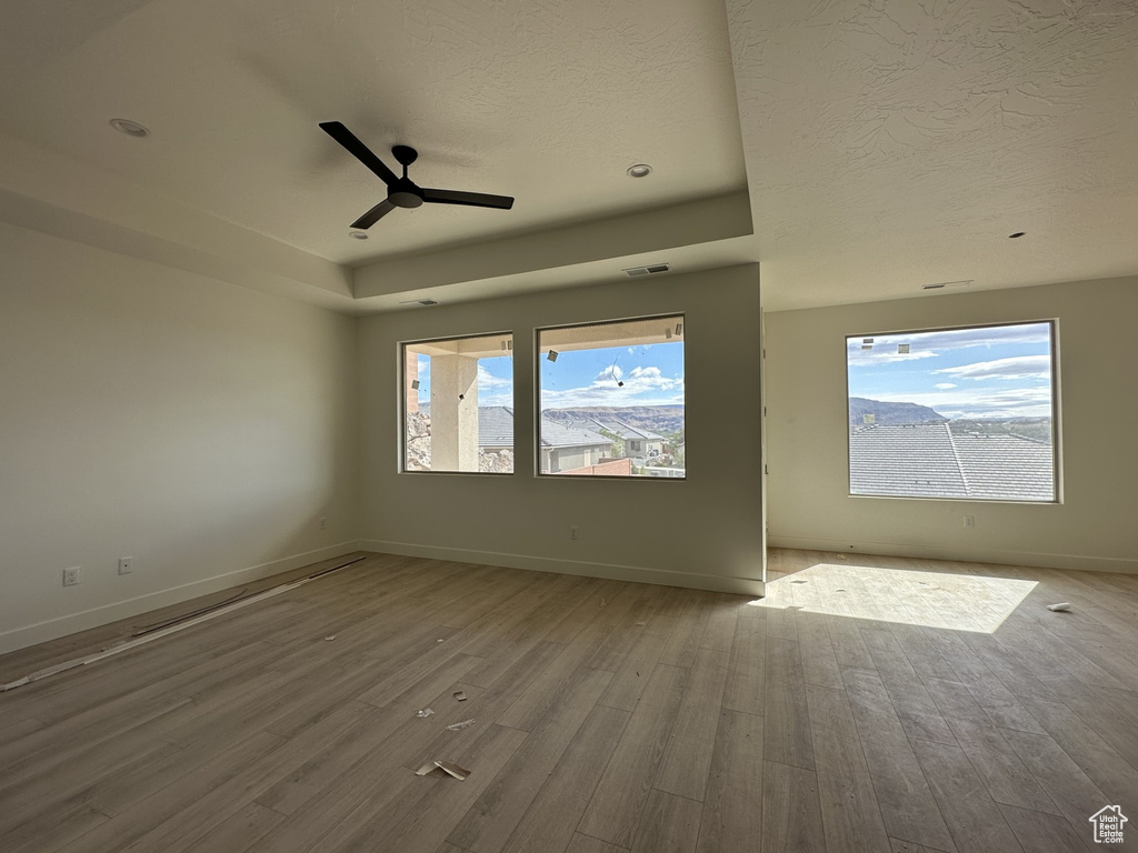 Empty room featuring ceiling fan, a textured ceiling, wood-type flooring, and a wealth of natural light