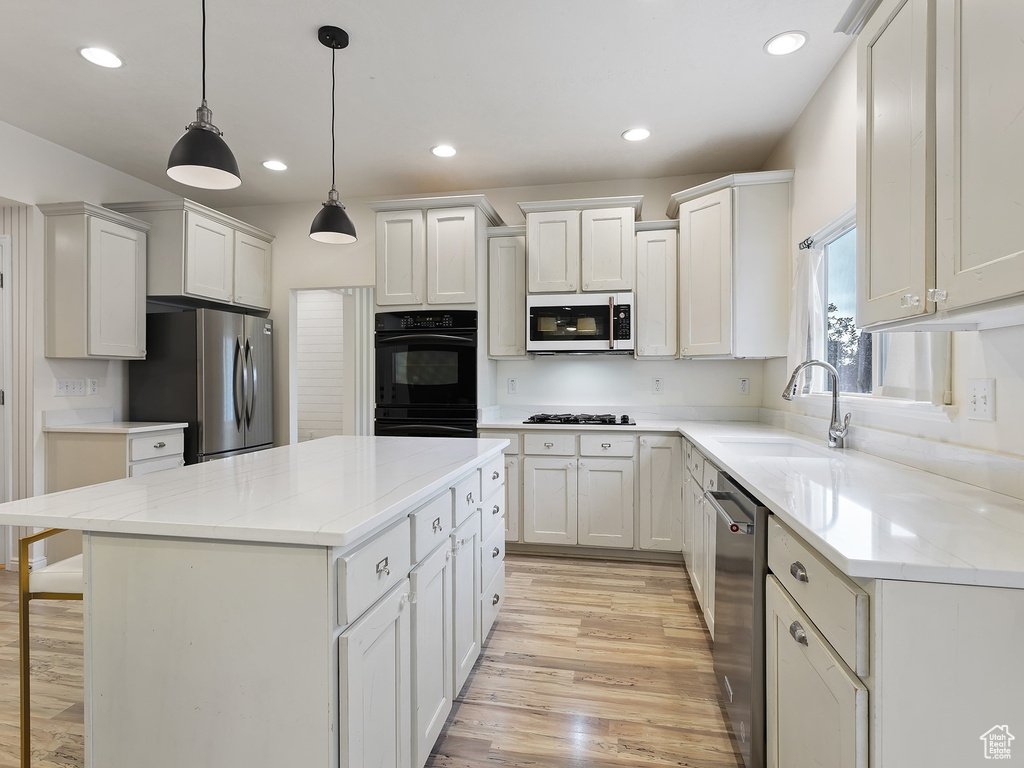 Kitchen featuring decorative light fixtures, light wood-type flooring, black appliances, sink, and a kitchen island