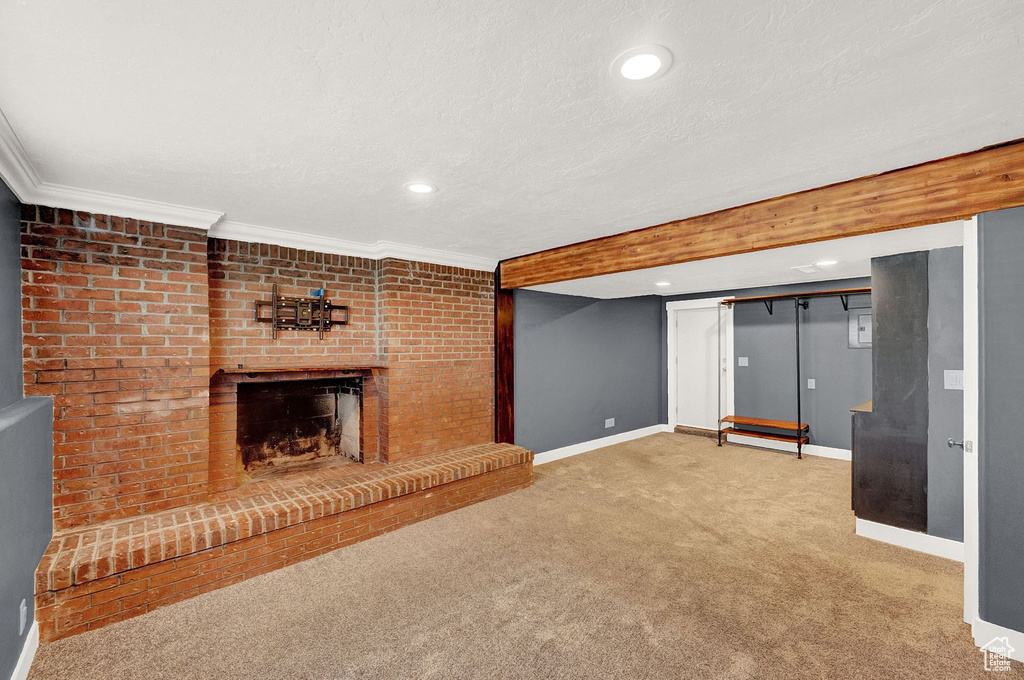Unfurnished living room featuring brick wall, a textured ceiling, a fireplace, carpet, and ornamental molding