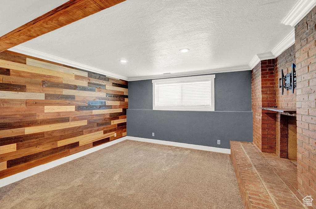 Empty room featuring a textured ceiling, wood walls, carpet, and crown molding