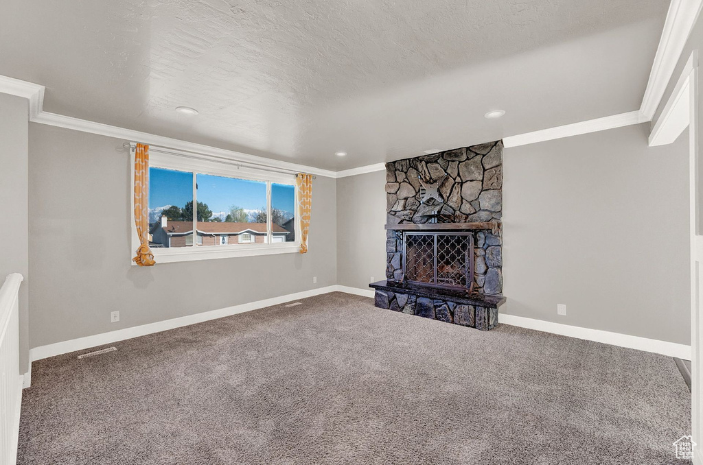 Unfurnished living room featuring a textured ceiling, ornamental molding, carpet, and a stone fireplace