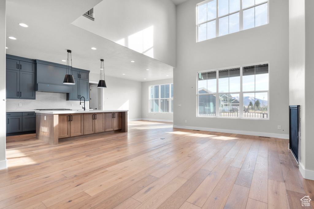 Kitchen featuring hanging light fixtures, light hardwood / wood-style flooring, tasteful backsplash, and a kitchen island with sink