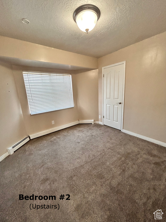 Carpeted empty room featuring a textured ceiling and baseboard heating