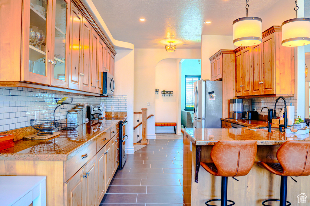 Kitchen featuring kitchen peninsula, backsplash, appliances with stainless steel finishes, sink, and pendant lighting