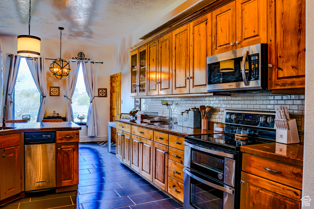 Kitchen featuring decorative light fixtures, backsplash, stainless steel appliances, a textured ceiling, and a notable chandelier
