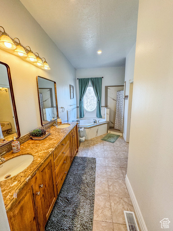 Bathroom featuring double sink vanity, tile floors, a bathing tub, and a textured ceiling