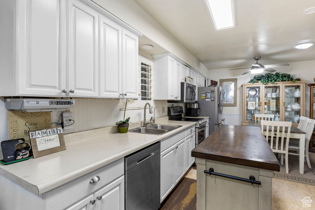 Kitchen with light tile flooring, white cabinetry, appliances with stainless steel finishes, sink, and ceiling fan