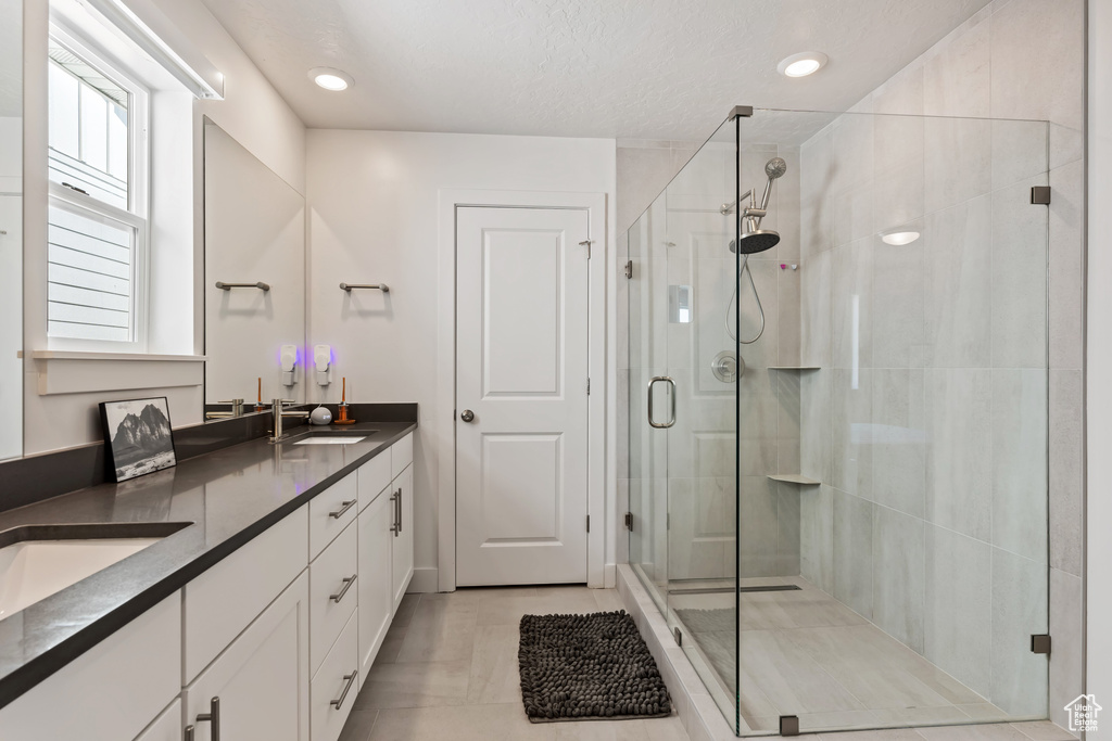 Bathroom with walk in shower, vanity with extensive cabinet space, double sink, and tile flooring