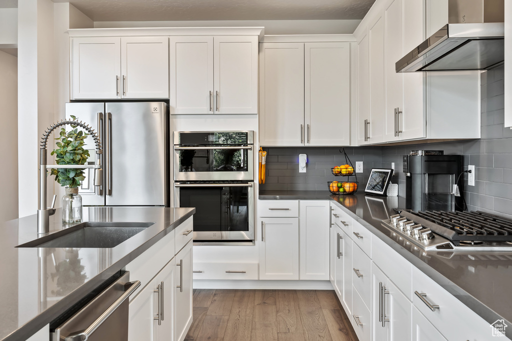 Kitchen featuring stainless steel appliances, light hardwood / wood-style floors, tasteful backsplash, wall chimney exhaust hood, and white cabinetry