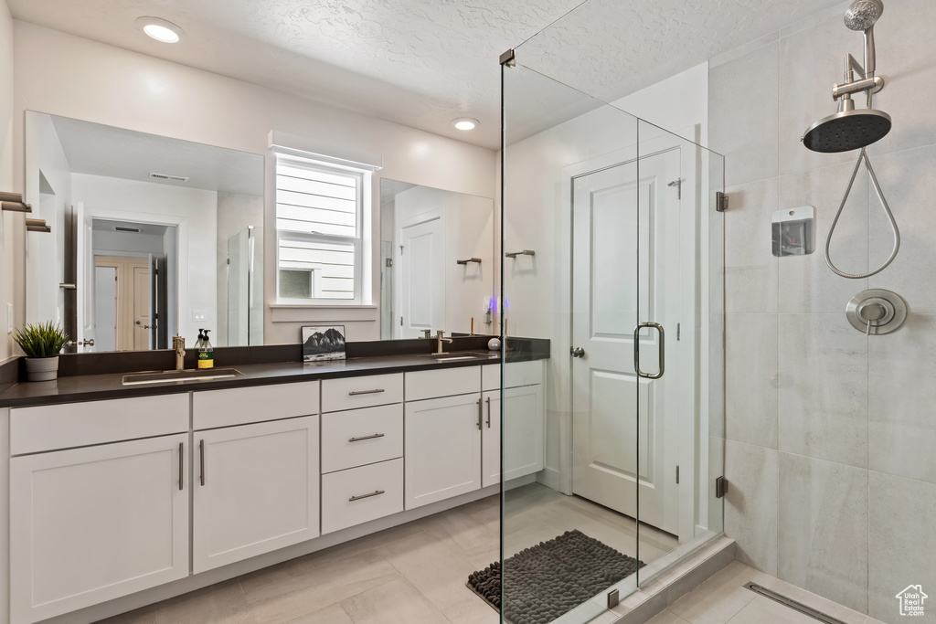 Bathroom featuring tile flooring, dual sinks, vanity with extensive cabinet space, and a shower with shower door