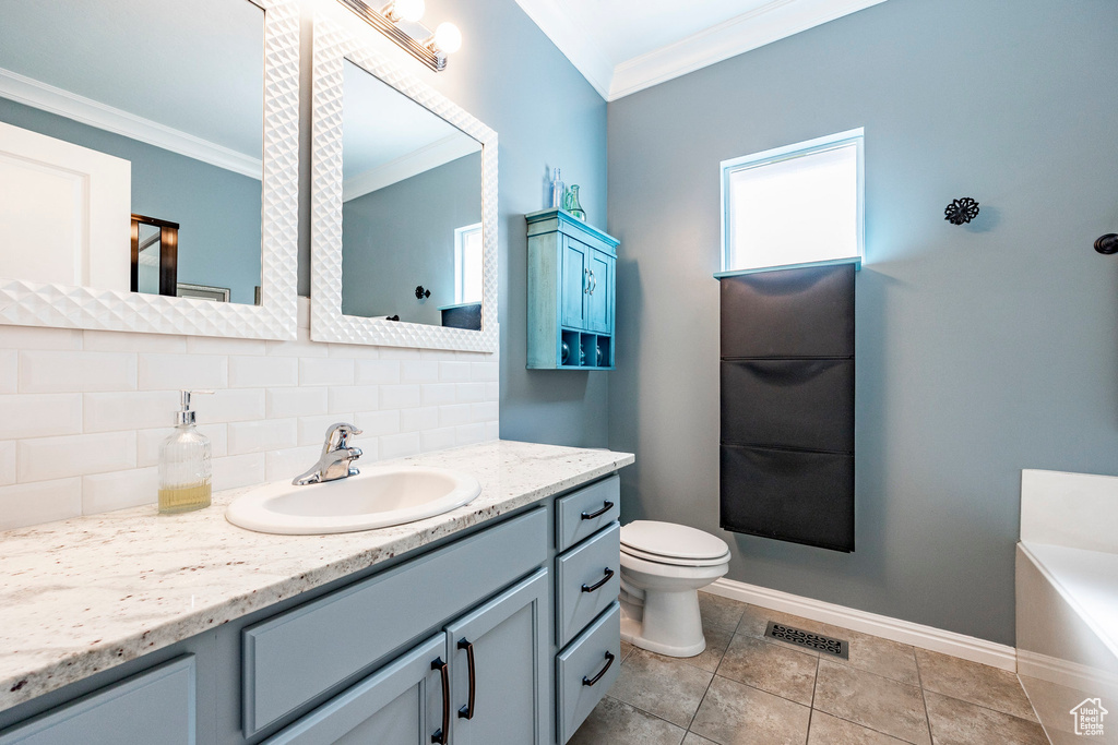 Bathroom with backsplash, toilet, vanity with extensive cabinet space, tile floors, and ornamental molding