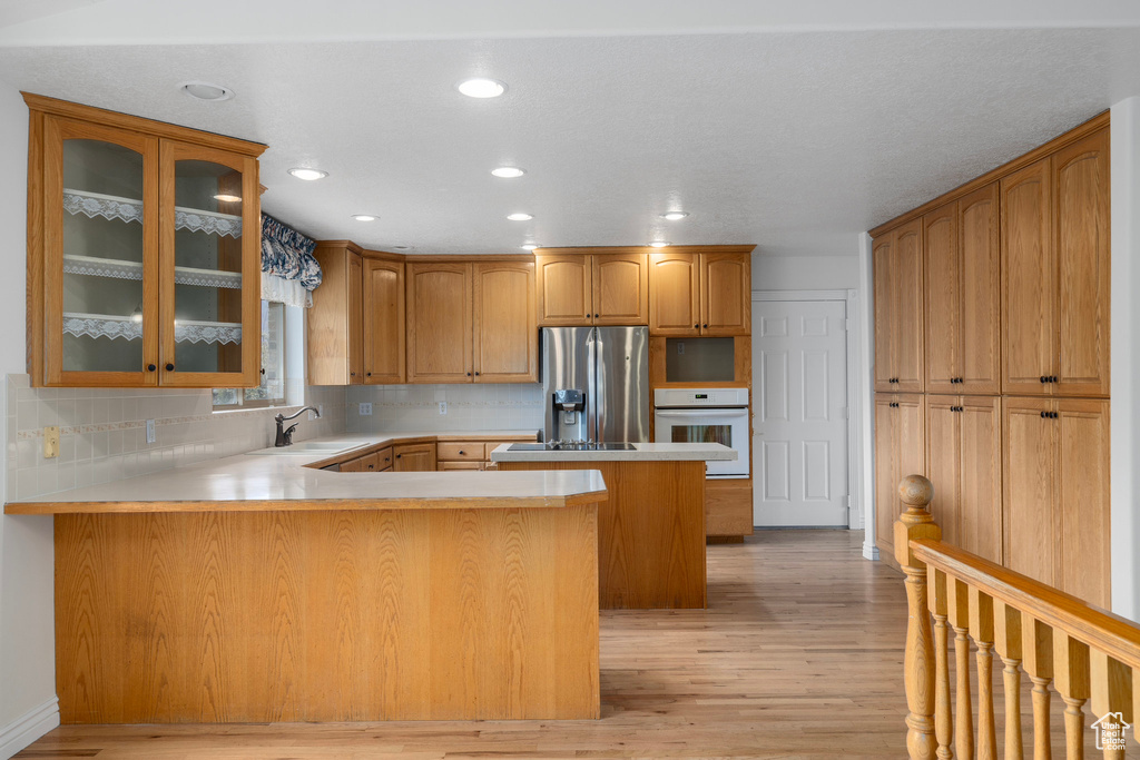 Kitchen featuring oven, sink, light hardwood / wood-style floors, stainless steel fridge, and kitchen peninsula