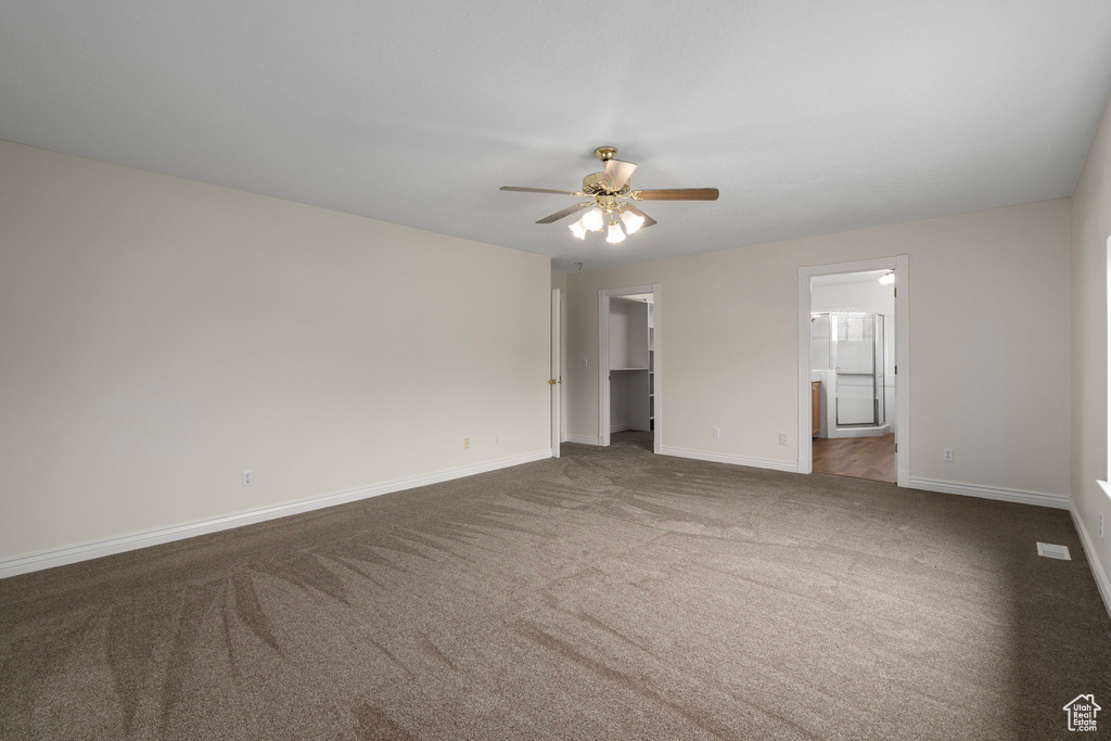Unfurnished bedroom with ensuite bath, ceiling fan, dark carpet, and a walk in closet