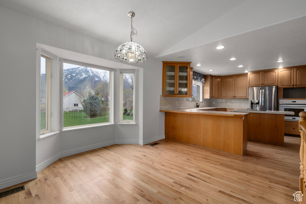 Kitchen with decorative light fixtures, light hardwood / wood-style flooring, white oven, tasteful backsplash, and stainless steel fridge