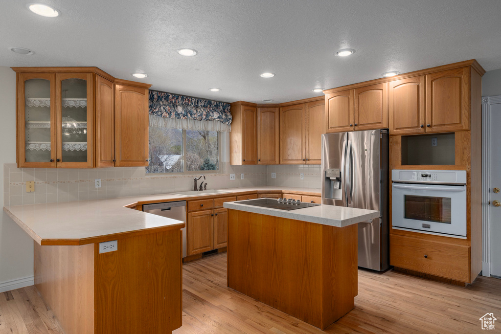 Kitchen featuring backsplash, appliances with stainless steel finishes, sink, a kitchen island, and light hardwood / wood-style floors