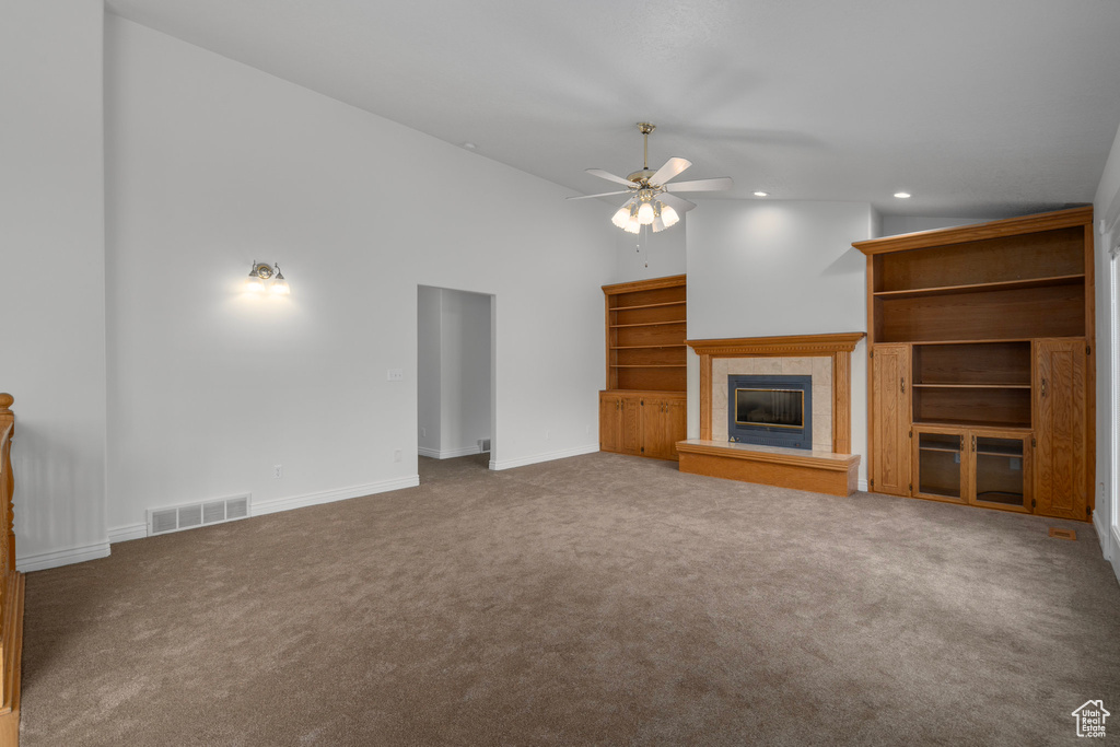 Unfurnished living room with high vaulted ceiling, a tile fireplace, ceiling fan, and carpet floors
