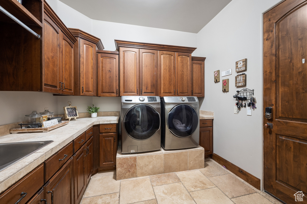 Washroom featuring washer and dryer, cabinets, and light tile floors