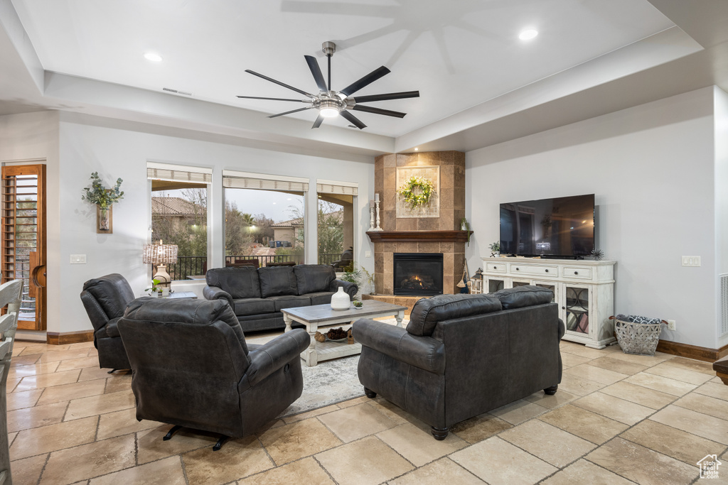 Living room featuring ceiling fan, a raised ceiling, a fireplace, and a wealth of natural light