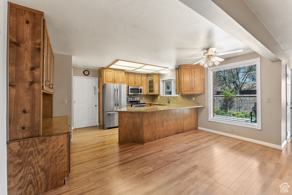 Kitchen with kitchen peninsula, appliances with stainless steel finishes, ceiling fan, light hardwood / wood-style floors, and sink