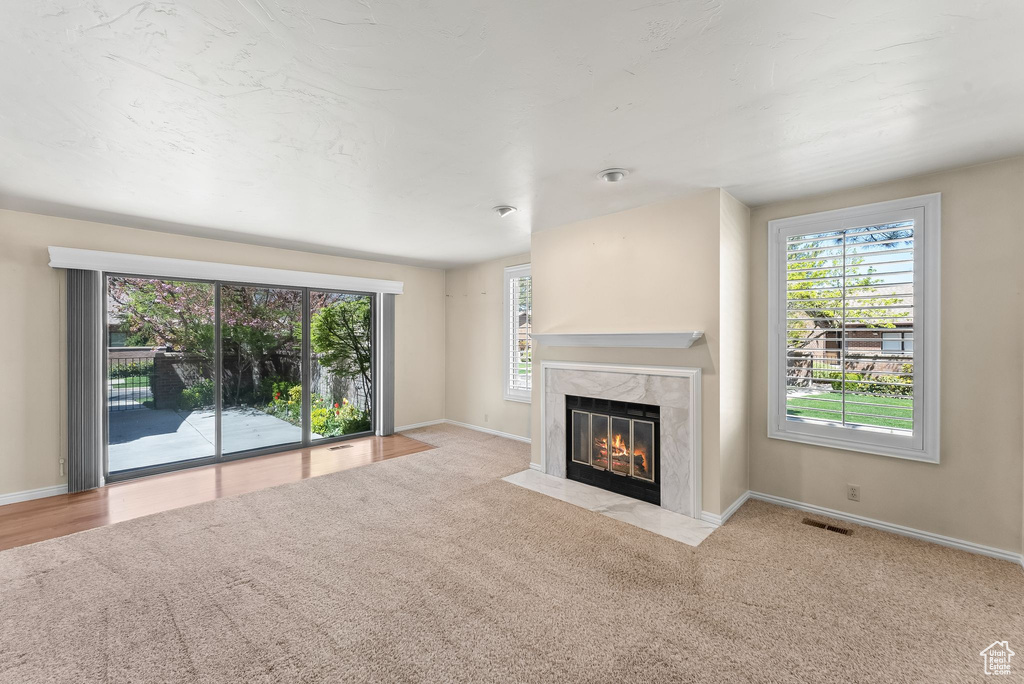 Unfurnished living room with a wealth of natural light, a premium fireplace, and light colored carpet