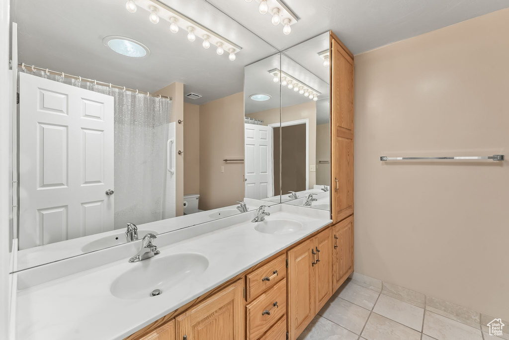 Bathroom with toilet, tile floors, and dual vanity
