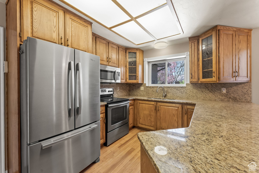 Kitchen featuring light stone counters, appliances with stainless steel finishes, sink, backsplash, and light hardwood / wood-style flooring