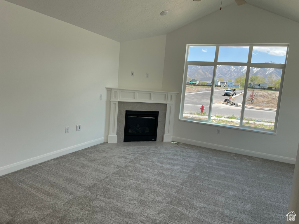 Unfurnished living room featuring carpet floors, a tile fireplace, and vaulted ceiling