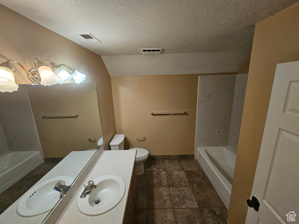 Full bathroom with tiled shower / bath combo, vanity, tile flooring, toilet, and a textured ceiling