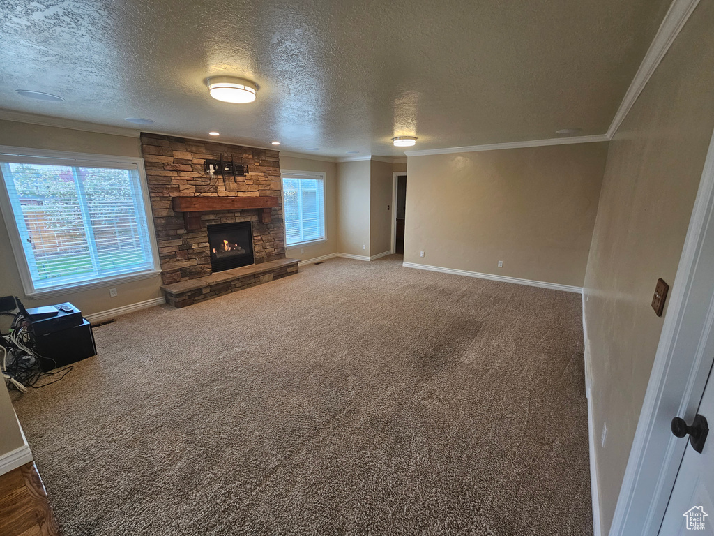 Unfurnished living room with a healthy amount of sunlight, a textured ceiling, dark colored carpet, and a stone fireplace