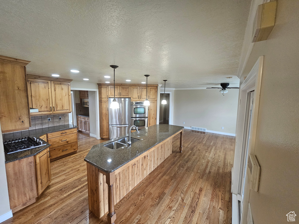 Kitchen featuring backsplash, stainless steel appliances, hardwood / wood-style floors, sink, and pendant lighting