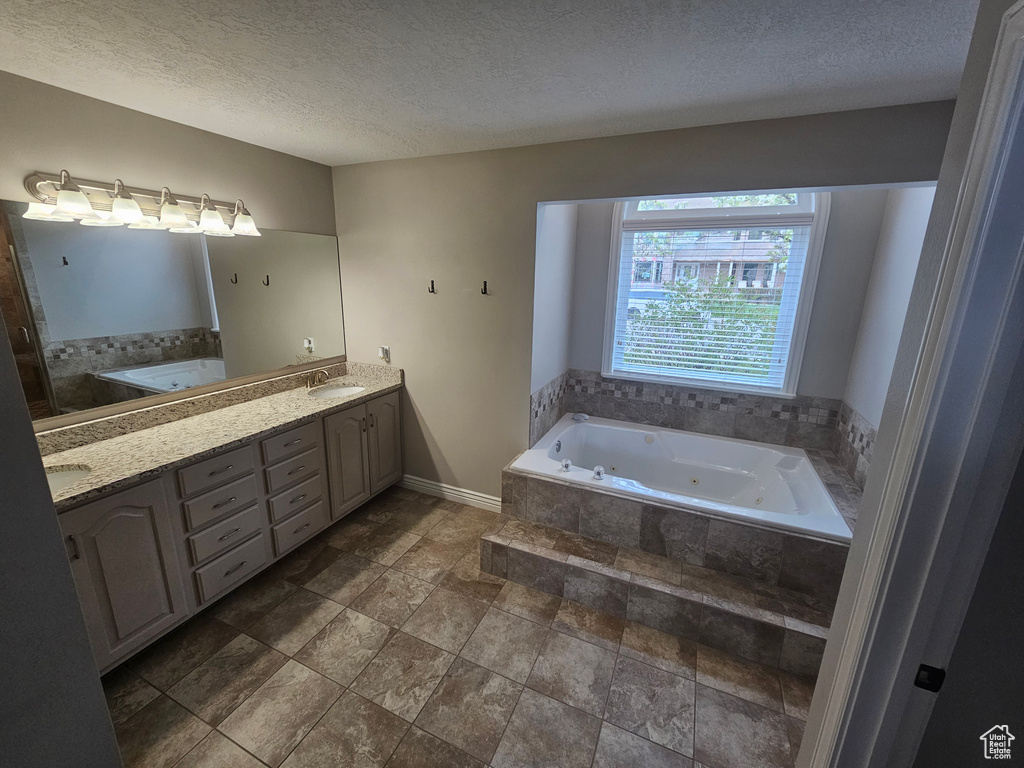 Bathroom featuring a textured ceiling, tile floors, double vanity, and tiled tub