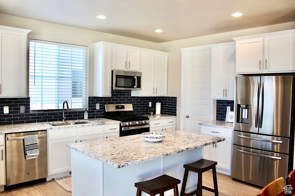 Kitchen with light wood-type flooring, a center island, tasteful backsplash, and stainless steel appliances