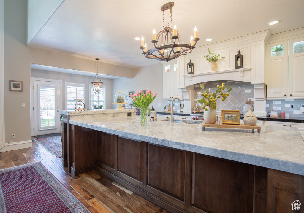 Kitchen with light stone counters, white cabinets, tasteful backsplash, dark wood-type flooring, and pendant lighting