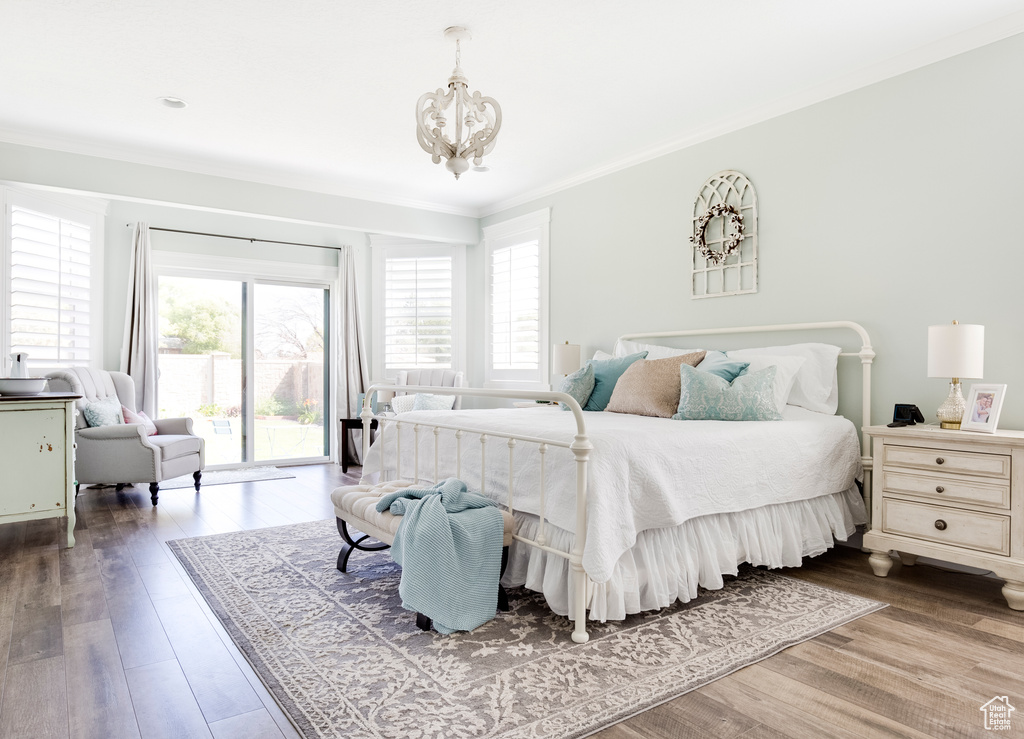 Bedroom featuring hardwood / wood-style floors, ornamental molding, access to outside, and an inviting chandelier