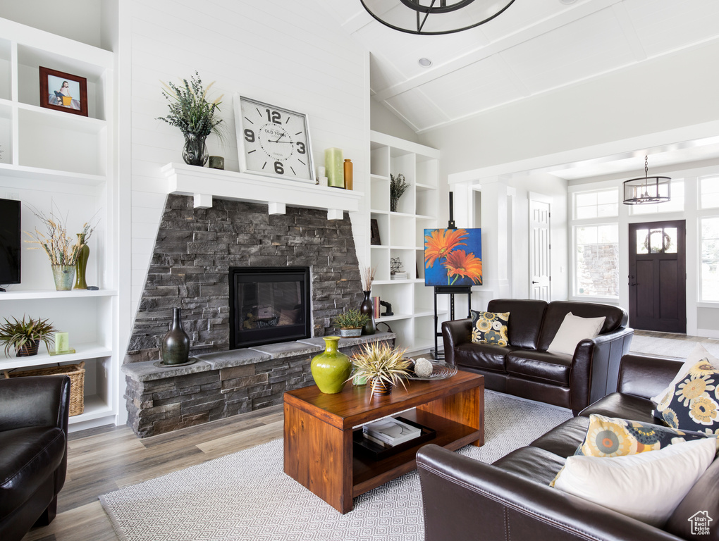 Living room featuring built in features, a stone fireplace, vaulted ceiling, and hardwood / wood-style floors