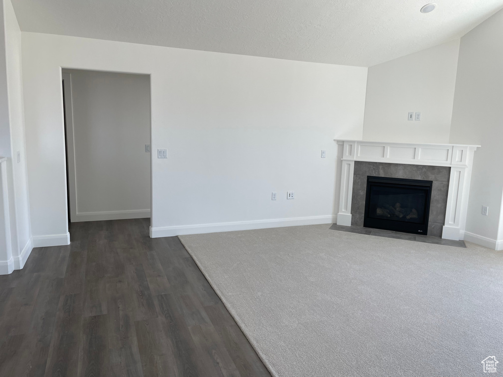 Unfurnished living room with lofted ceiling, dark carpet, and a fireplace